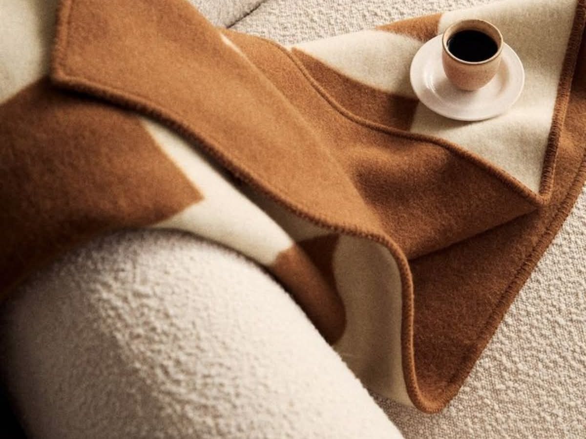 Camel and ivory reversible wool throw folded over a bouclé armchair beside a coffee cup