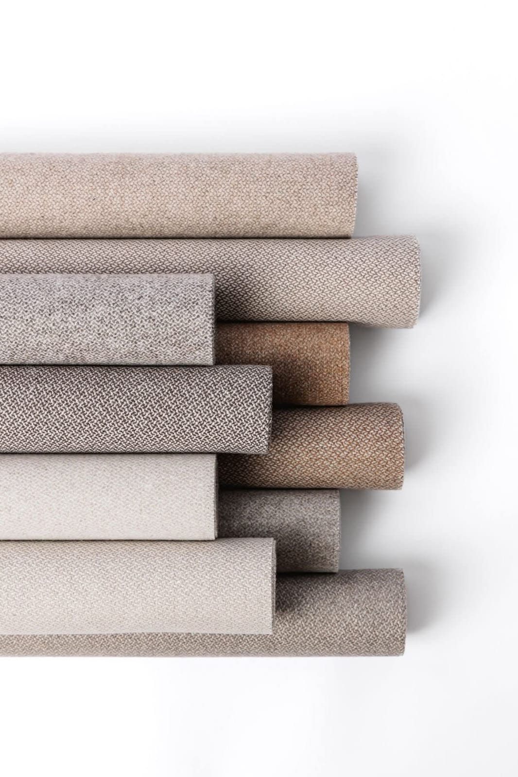Stacked rolls of neutral upholstery fabric in bouclé, herringbone and plain weaves